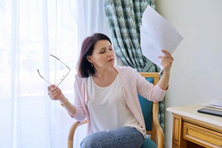 mature-woman-with-closed-eyes-waving-papers-suffering-from-heat
